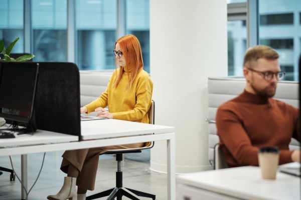 A woman in a yellow jumper and a man in an orange jumper working on computers in an office