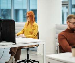 A woman in a yellow jumper and a man in an orange jumper working on computers in an office