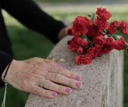 A bereaved woman with her hand on a gravestone while holding a bunch of red flowers