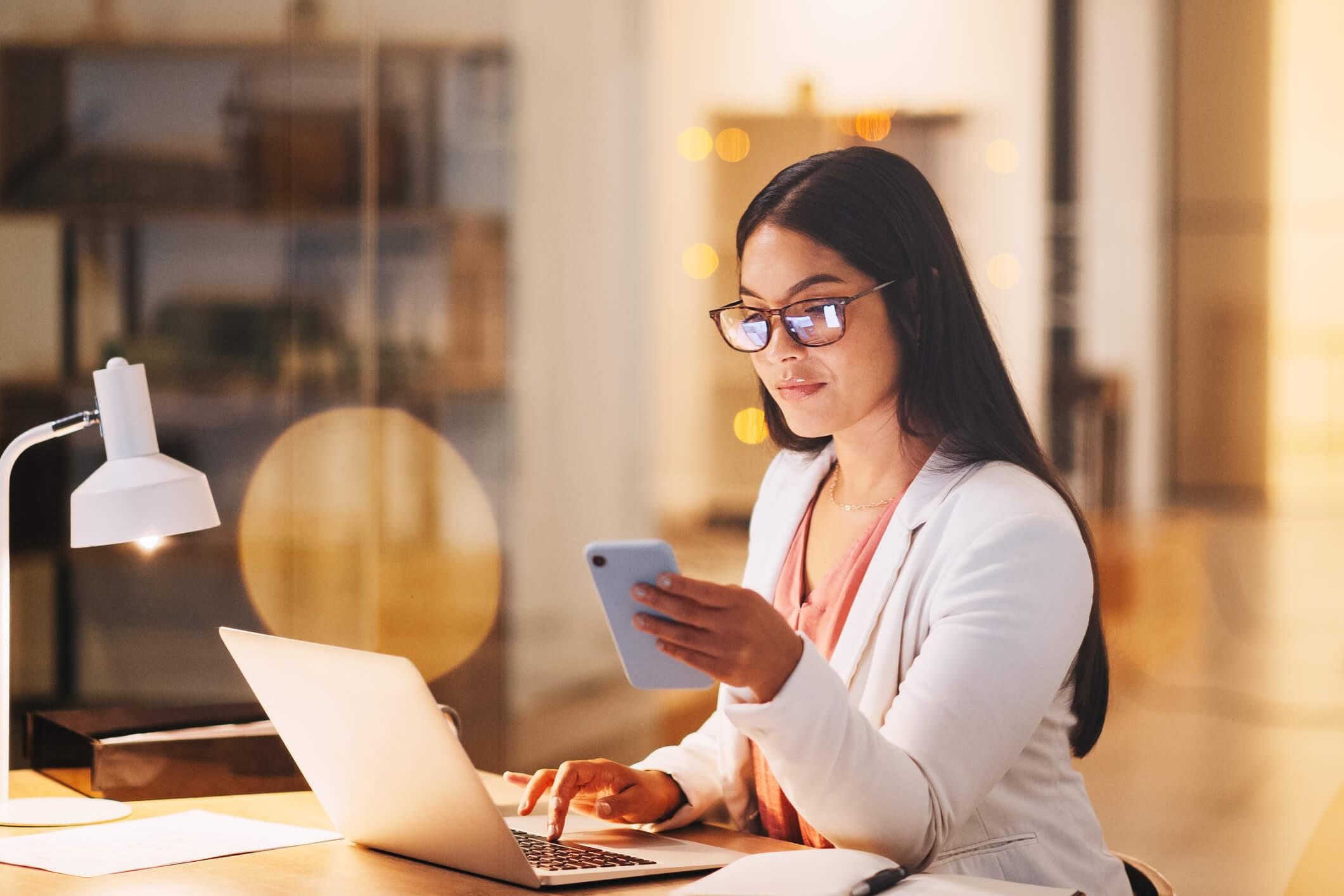 Woman working on laptop and checking social media on phone